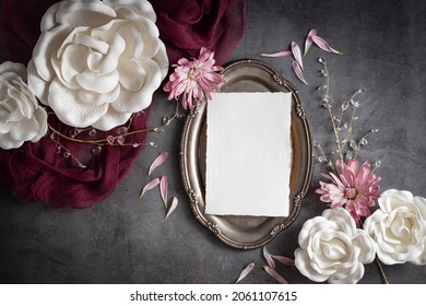 Moody Burgandy floral display overhead flat lay with vintage paper on silver tray against gray background.
