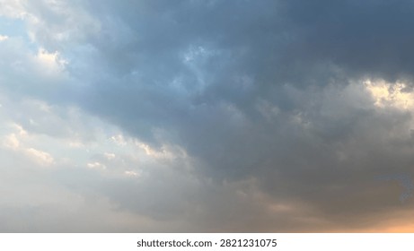 A moody and dramatic cloudy sky showing dark rain clouds mixed with soft golden sunset light breaking through the lower horizon. The contrasting blue grey clouds and warm sunlight create a atmospheric and artistic sky background. Perfect for nature backgrounds, weather forecasts, dramatic design backdrops, spirituality themes, and artistic overlay effects.