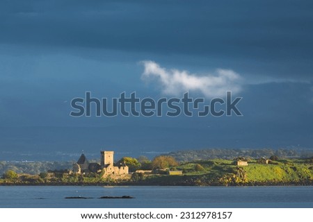 Moody, dramatic view of golden light over the Firth of Forth onto the historic medieval monastery Incholm Abbey, from Aberdour, Fife, Scotland, UK.