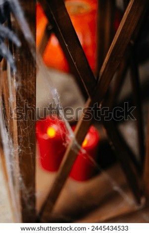 A moody Halloween scene with red candles behind cobwebs, creating a mysterious and spooky atmosphere in a dim setting.