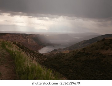 A moody landscape of misty mountains, red rock cliffs, and a calm lake nestled in a vast valley. Soft, diffused light and clouds enhance the tranquil, dramatic atmosphere. - Powered by Shutterstock