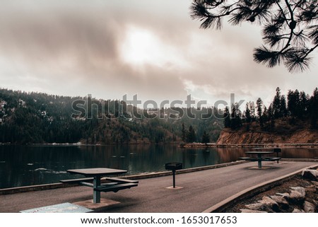 Moody landscape with picnic benches, mountains, and a lake.