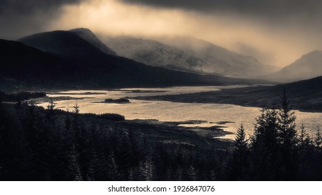 Moody landscape scenery in Scotland.Sun shining through the dark and heavy clouds over scenic mountain valley and Loch Loyne in Scottish Highlands. The old photograph look made with a sepia effect.
