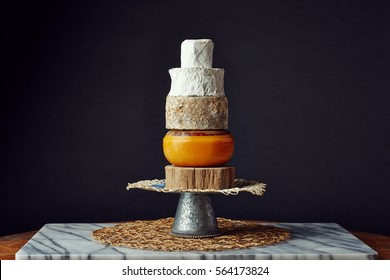 moody photo of a tower of cheese wheels on a slice of wood - Powered by Shutterstock