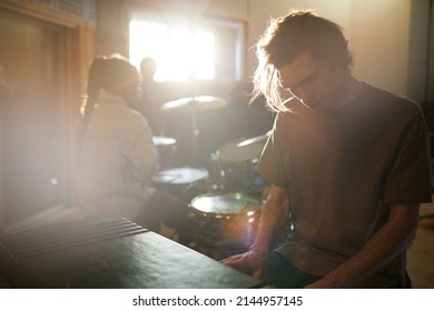 Moody portrait of long haired young man playing music rehearsing with band in dim sunlight, copy space