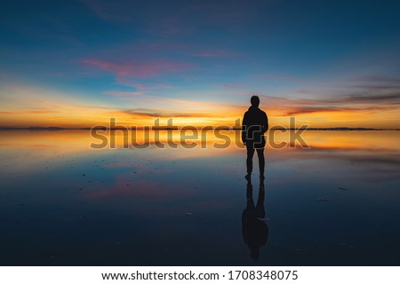Moody shot of man looking into the horizon at dawn, solo traveller watching the sunrise at Uyuni Salt Flats (Spanish: Salar de Uyuni ), Bolivia, South America.