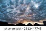 Moody sky with dramatic, textured clouds at sunset, silhouetted rooftops of houses in the foreground, capturing a captivating evening scene