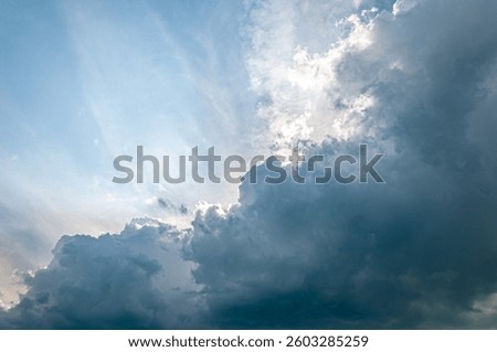 Moody sky with sun rays piercing through thick, dark storm clouds. A powerful atmospheric scene capturing the calm before a summer thunderstorm. Perfect for backgrounds or weather themes.
