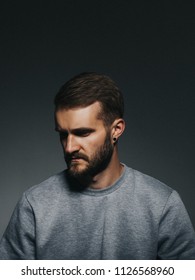 Moody Studio Portrait Of A Young Man With Beard Looking Away From Camera With Serious Face. Wearing Grey Sweatshirt. Copy Space.