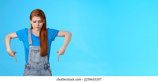 Moody upset cute redhead woman feel uneasy, frowning look pointing up jealousy and regret, cannot afford awesome new product, express sadness and sorrow, stand blue background gloomy. - Shutterstock ID 2239655197