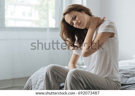 Moody young woman holding her neck