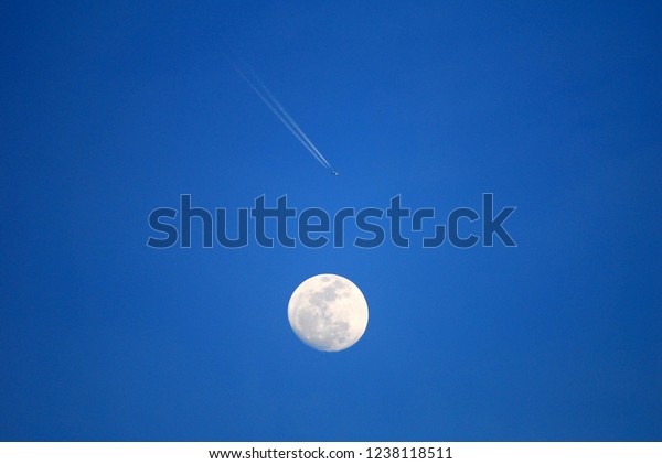The moon and the airplane with smoke and blue\
sky background