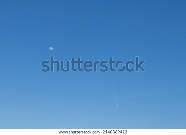Moon and Airplane Trail on a Bright Blue Sky.\
The concept of Nature and\
Technology.