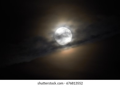 The moon appears in the night behind a cloud.