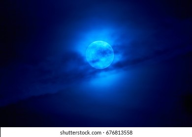 The moon appears in the night behind a cloud.