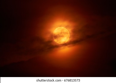 The moon appears in the night behind a cloud.