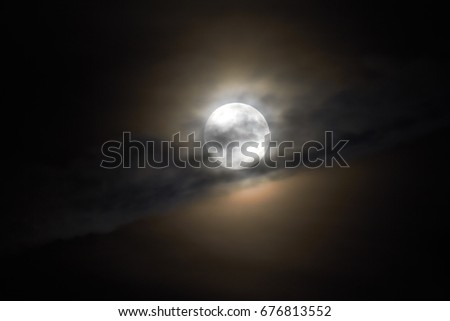 The moon appears in the night behind a cloud.