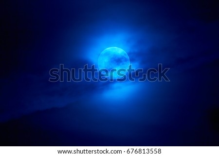 The moon appears in the night behind a cloud.
