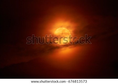 The moon appears in the night behind a cloud.