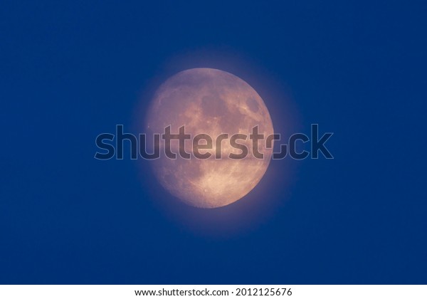 Moon in atmospheric\
haze against blue sky.