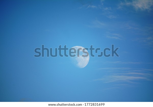 Moon in the\
daytime, blue sky with small\
clouds
