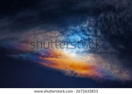 the moon, a dramatic sky featuring a vivid rainbow-like gradient stretching horizontally across the image with dense, textured gray clouds, while the lower portion transitions into a dark