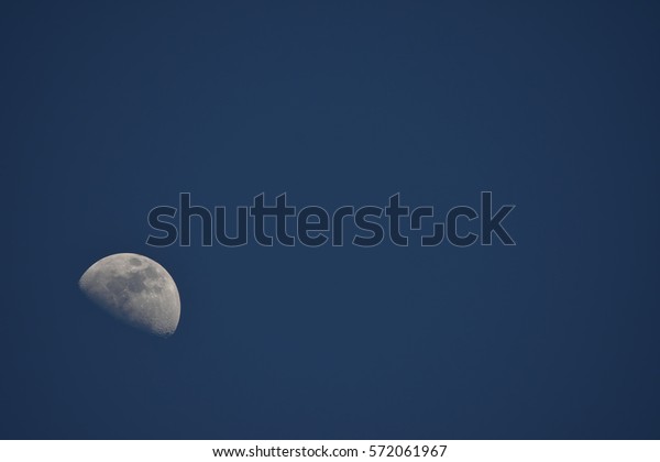 Moon During Day in Blue Sky.\
Bright moon orbiting earth in a blue clear sky during the\
daytime