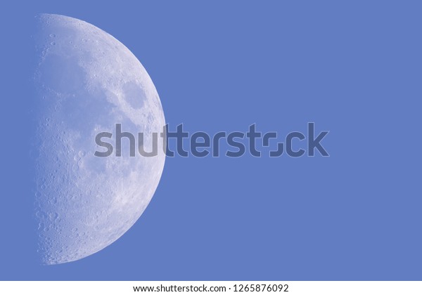 Moon in the first quarter phase in the evening blue\
sky. The right hemisphere of the natural Earth satellite in the\
left part of the image