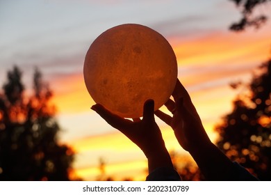  Moon In The Hand On Red Sunrise Background. Moon Bedside Lamp On The Sky                              