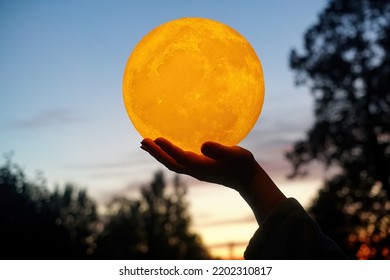  Moon In The Hand On Red Sunrise Background. Moon Bedside Lamp On The Sky                              