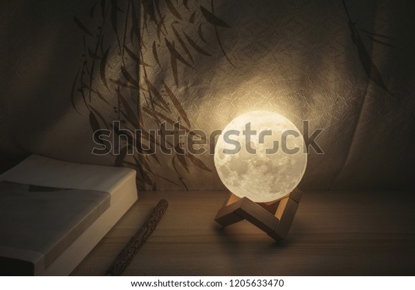 Moon lamp on desk, light at night, reading book on\
wooden table, with Chinese blinds and wooden pencil and moonlight.\
with copy space 