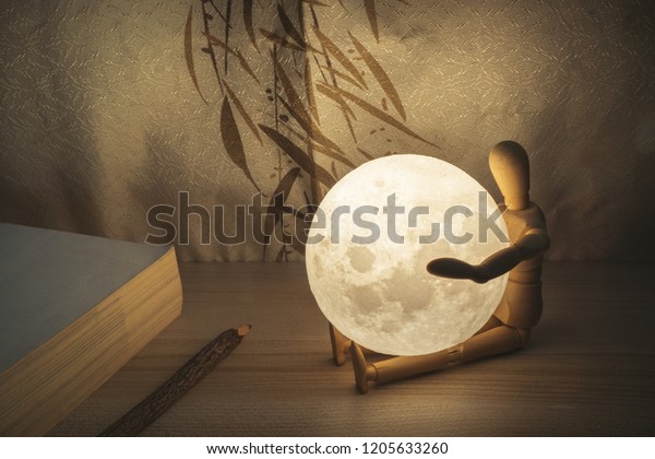 Moon lamp on desk, wooden doll hug the Moon, light\
at night, reading book on wooden table, with Chinese blinds and\
wooden pencil