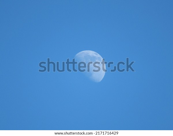 The Moon is a natural satellite of\
the Earth.  First quarter.  Close-up.  Blue\
sky.