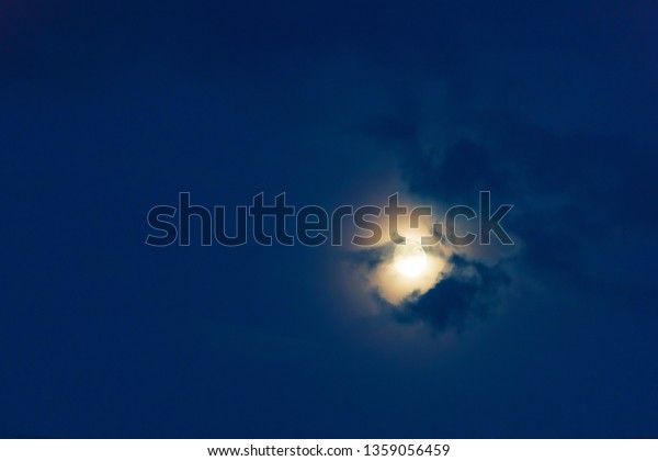 Moon in the night cloudy sky.\
Night time. Yellow glowing moon in the sky. Cloudy sky at\
night.