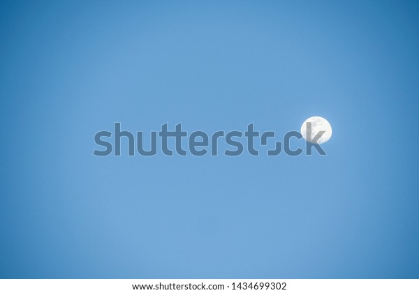 A moon at\
noon in the background of a blue\
sky