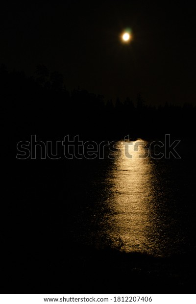 Moon path on a black night on the calm water\
of Lake Ladoga among rocks in\
Karelia