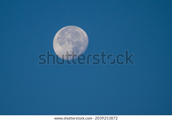 The moon photographed during the day. The moon\
on a blue background
