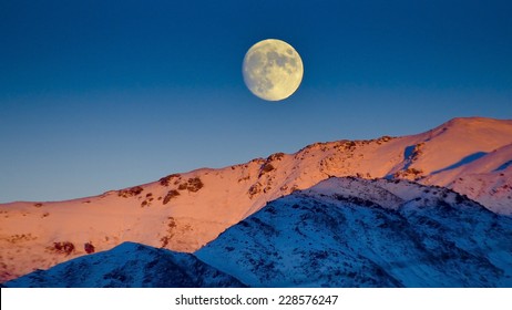 Moon rises over snow capped mountains at twilight - Powered by Shutterstock