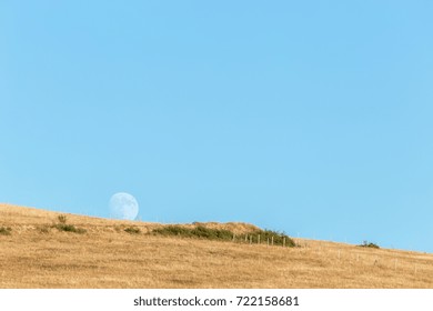 Moon rising up behind an hill, with an empty, blue sky