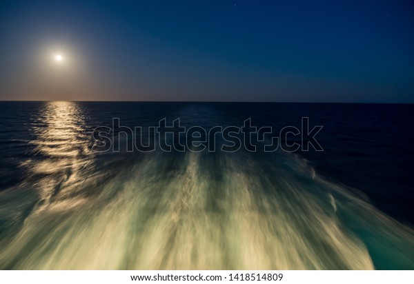 Moon rising over wake and waves\
of cruise ship at sea with concept of leaving or starting\
anew