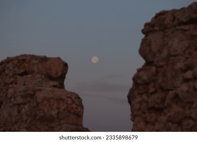 A moon sets between the columns of a Byzantine ruin in dim light