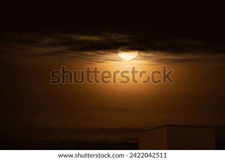 The Moon in the sky in dark clouds surrounded by yellow light is a multiple moonlight in the atmosphere. Full moon in the style of mystical and thriller films