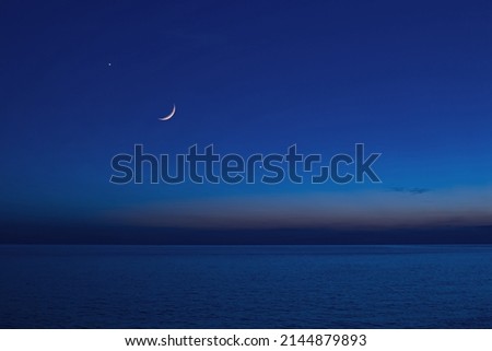 Moon with starry skies and planets above ocean horizon.