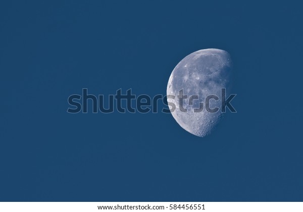 The Moon in a Waning Gibbous\
Phase in dark blue sky in early morning, showing detailed\
craters