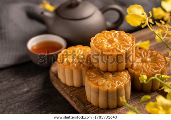 Mooncake, Moon cake for Mid-Autumn Festival,\
concept of traditional festive food on black slate table with tea\
and yellow flower, close up, copy\
space.
