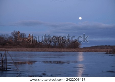A moonlit path on the lake, in the middle of the reeds, in late autumn. An abandoned, ruined church on the other side of the lake