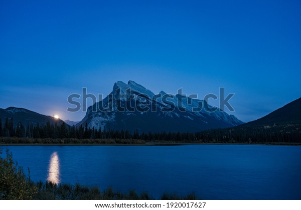 Moonrise at Vermilion Lakes in summer night.\
Banff National Park, Canadian Rockies, Alberta, Canada. Bright full\
moon over Mount Rundle and light up the night with golden\
reflection on lake\
surface.