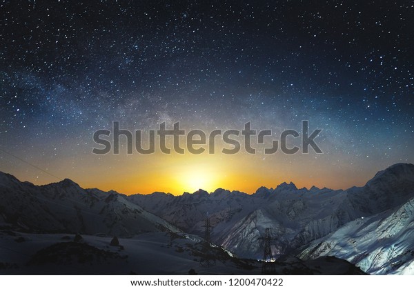 Moonset in the\
mountains at night with a horizontal milky way on the sky. Snow\
covered peaks of mountains at\
night