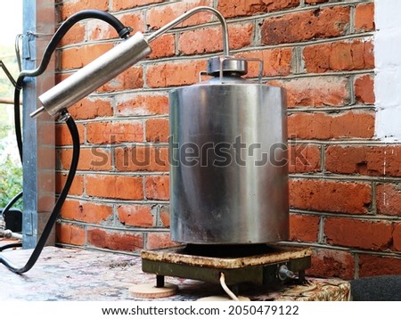 moonshine still standing on an old heating plate against a brick wall background, production of alcohol at home using distillation equipment, home distiller in a rural yard