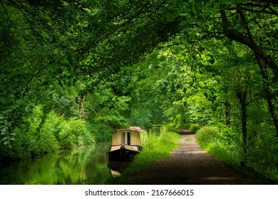 A moored barge rests peacefully on a canal in the beautiful Welsh countryside. lush green verdant trees grow in abundance in the pleasant natural surroundings of the Brecon and Monmouth canal
